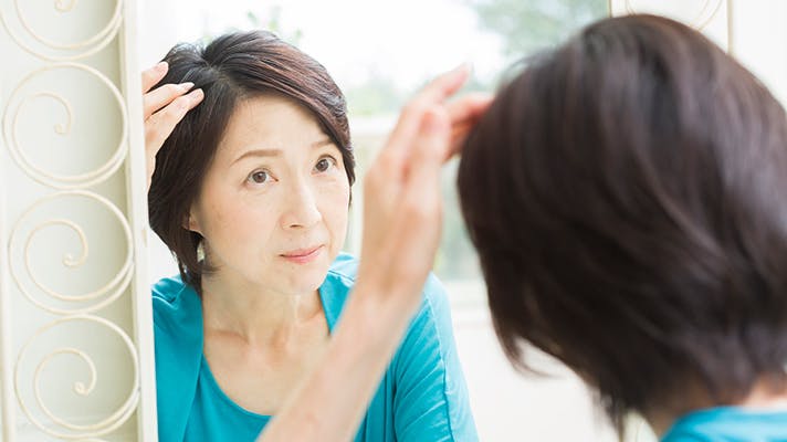 鏡で髪を確認する女性